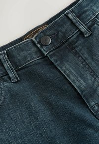 Mörka denimjeans med en klassisk femfickdesign, knäppning och kontrasterande sömmar längs midjan och sömmarna.