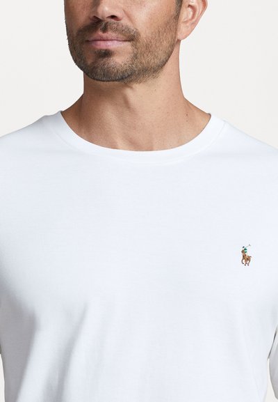 Tricou alb din bumbac cu gât rotund, având un mic logo brodat cu un cal și un cavaler în nuanțe de brun și verde pe partea stângă a pieptului.