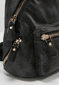 Gros plan sur le coin d’un sac noir texturé avec deux fermetures éclair métalliques dorées et des curseurs en cuir noir.