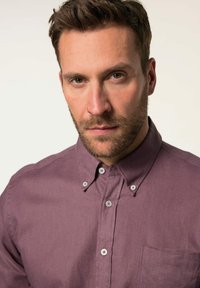 Chemise à boutons dans un tissu violet doux, dotée d'un col, d'une poche poitrine et de boutons gris, avec une surface texturée.