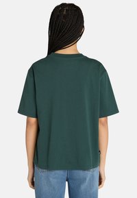 Grünes Baumwoll-T-Shirt mit Rundhalsausschnitt, kurzen Ärmeln und lockerer Passform. Die Rückansicht zeigt eine glatte Textur und minimalistische Designdetails.
