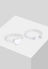 Două inele din argint, unul cu un design în formă de inimă și celălalt cu un accent de piatră rotundă. Ambele au un finisaj neted și lustruit.