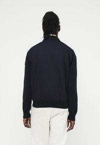 Μπλε σκούρα μπουφάν τύπου βόμβερ με πλεκτή υφή για το γιακά και τις μανσέτες, με απαλό και λείας υφής σώμα και ριμπ τελείωμα, εμφανιζόμενο από πίσω.