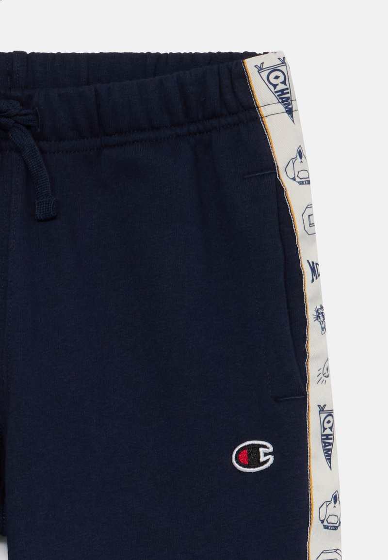 Pantaloni jogger navy in cotone con vita elasticizzata e cordino. Tasche laterali con stampe e dettagli del logo.
