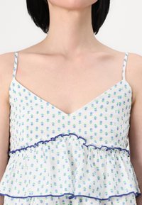 Vestido floral blanco con estampados azules y verdes, escote en v, tirantes finos, dobladillo con volantes y ribete azul marino. Tejido ligero.