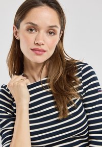 Maglietta a maniche lunghe a righe blu navy e bianche con scollatura tonda. Tessuto morbido e liscio; design aderente. Il modello tiene il tessuto all'altezza della scollatura.