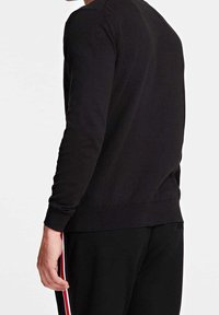 Musta pitkähihaisen neuleen ribbikuvio, jossa pyöreä kaula-aukko ja tiukat hihat, yhdistettynä mustiin housuihin, joissa on punaiset sivusuunnat.