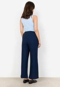 Marineblauwe wijde broek van een gestructureerde stof, met een hoge taille en een uitlopende zoom. Gepaard met een lichtblauw tanktop en zwarte schoenen.