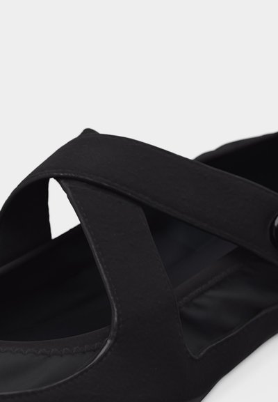 Μαύρο φλατ σανδάλι με φαρδιές σταυρωτές υφασμάτινες λουρίδες και επενδεδυμένη σόλα, σχεδιασμένο για καθημερινή χρήση.