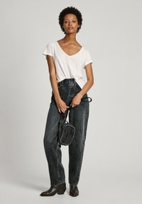 Balta V formos iškirpte marškinėliai, aukštai juosmeniui pritaikyti tamsūs džinsai, rudų kulkšnies botai ir maža juoda per petį nešama rankinė. Paprastas dizainas, minkšta tekstūra.