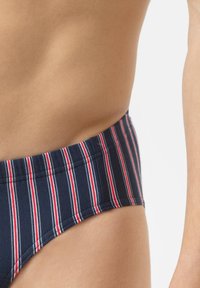 Marineblauwe zwemslip met horizontale rode en witte strepen op de tailleband, gemaakt van gladde stof, met een strakke pasvorm en een minimalistisch ontwerp.