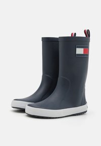 Bottes en caoutchouc de couleur marine avec des semelles blanches, ornées d'un détail en forme de drapeau rectangulaire rouge, blanc et bleu sur le côté extérieur.