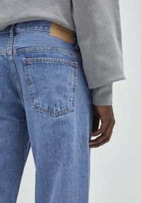 Jeans de mezclilla azules con un corte relajado, que presentan una etiqueta de cuero con la inscripción "PULL&BEAR" en la cinturilla. Bolsillo trasero con detalles de costura visibles.