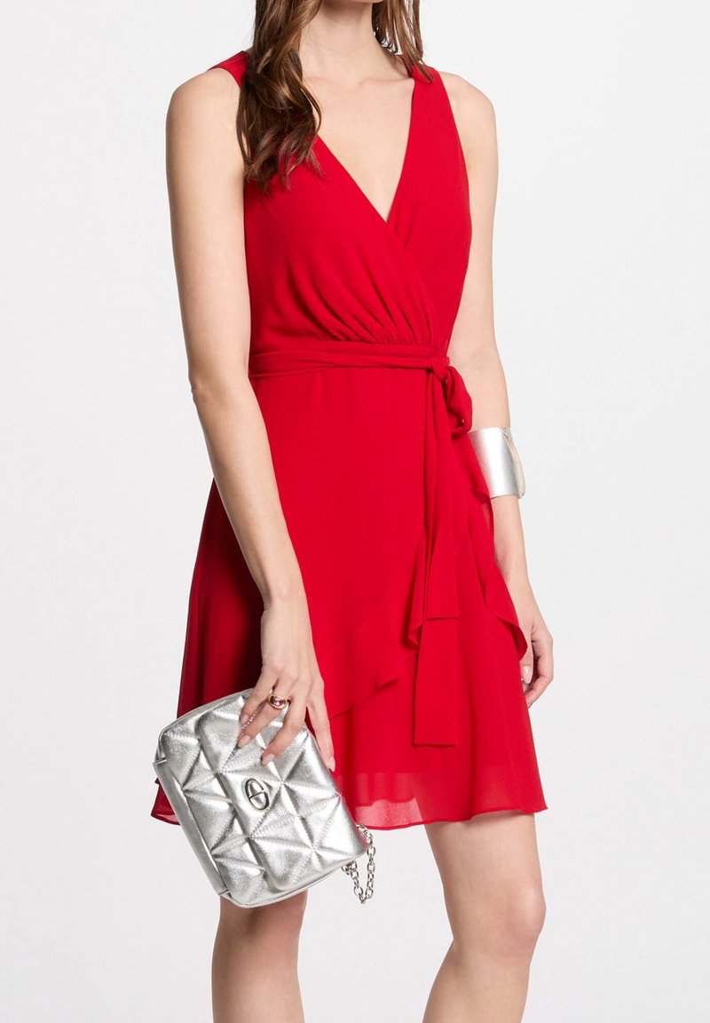 Robe portefeuille rouge avec un décolleté en V profond et des volants fluides. Associée à un sac à main matelassé argenté et un bracelet manchette argenté.