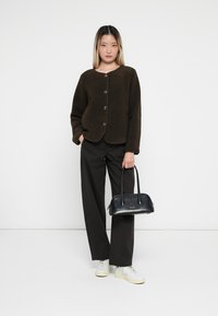 Brown fleece jacket with a round neckline and large buttons, paired with black wide-leg pants and a small black handbag. White sneakers.