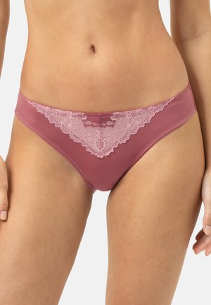 Femme portant un sous-vêtement style bikini mauve avec un détail en dentelle rose à l'avant, montré de la taille jusqu'au haut des cuisses sur fond blanc.