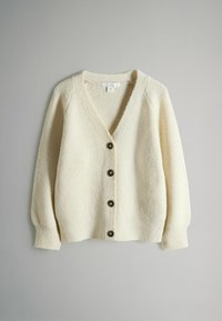 Kerman neule villatakki V-puolella, ribatusta tekstuurista ja kuudesta tummasta napista. Ominaisuuksiin kuuluvat pitkät, hieman puffatut hihat ja rento istuvuus.