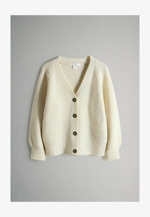 Kremni pleteni kardigan z V-izrezom, rebrasto teksturo in šestimi temnimi gumbi. Ima dolge, rahlo napihnjene rokave in sproščen kroj.