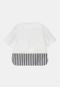 Top blanco de manga corta que presenta una tela texturizada con un dobladillo inferior de rayas en blanco y negro, escote redondeado y un corte relajado.