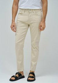 Pantalones rectos beige hechos de una tela suave, con un diseño tradicional de cinco bolsillos y una cremallera con cierre de botón.