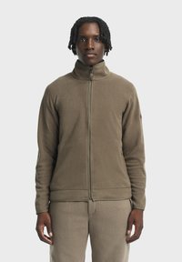 Fleece-Reißverschlussjacke in olivgrün, mit einem hohen Kragen und glatter Textur. Kombiniert mit passenden gemusterten Hosen.