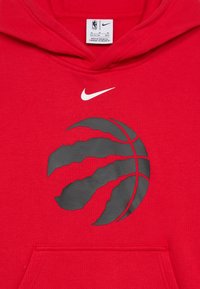 Czerwona bluza z kapturem z czarną grafiką koszykarską z rysami jakby od pazurów. Biały logo Nike znajduje się nad grafiką. Materiał wydaje się miękki i teksturowany.