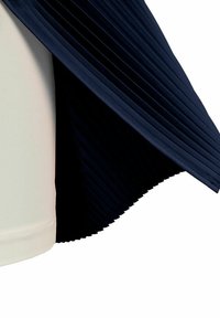 Drapado de tela plisada en color navy sobre una parte superior suave color crema. Los pliegues añaden textura, mientras que la base crema proporciona un contraste en color y diseño.