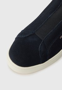 Adidași din suede bleu cu vârf rotund, panouri elastice laterale, talpă din cauciuc alb contrastant și detalii fine de cusătură.