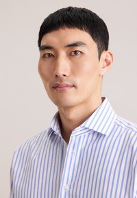 Koszula na guziki w białym kolorze z niebieskimi pionowymi paskami; posiada klasyczny kołnierz, zapięcie na guziki oraz gładką, bawełnianą tkaninę.