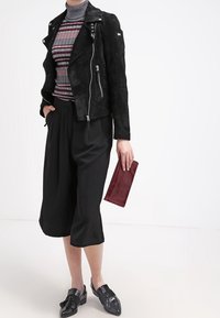 Svart mocka motorcykeljacka med silverdetaljer, randig polotröja, svarta vida byxor och glänsande svarta skor; håller en vinröd clutch.