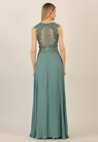 Long teal evening gown featuring intricate lace appliqué on a sheer back panel, flowing skirt, and a concealed zipper closure.