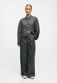 Veste oversized à rayures sombres avec des boutons, associée à un pantalon large assorti. Le tissu a une texture lisse. Fond blanc.
