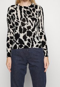 Black and cream long-sleeve top featuring an abstract animal print, crew neckline, soft texture, and slim fit, paired with dark denim pants.