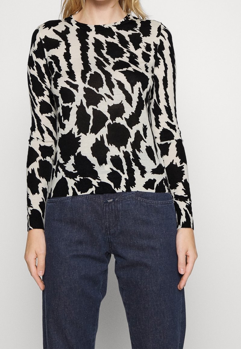Black and cream long-sleeve top featuring an abstract animal print, crew neckline, soft texture, and slim fit, paired with dark denim pants.