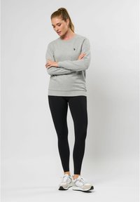 Grijze sweatshirt met geribde manchetten en zoom, met een klein logo. Draagt met zwarte leggings en lichtgekleurde sportschoenen.