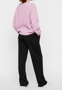Oversized, ribbed pink sweater paired with loose-fitting black trousers. The outfit features a relaxed silhouette and minimalistic white sneakers.