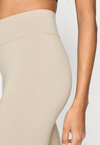 Μπεζ ψηλόμεσα κολάν με απαλή, ελαστική υφή. Διαθέτουν φαρδύ, άνετο κορδόνι μέσης και εφαρμοστή σιλουέτα.