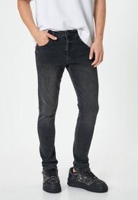 Svarta slim-fit jeans med en urtvättad finish, fem fickor och knappgylf. Bärs med texturerade svarta sneakers. Slät tygkvalitet.