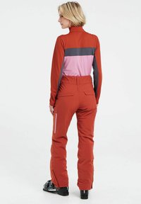 Completo da sci rosso e rosa con accenti grigi, design aderente, alto colletto e tasche con cerniera; presenta una vestibilità su misura e polsini regolabili.