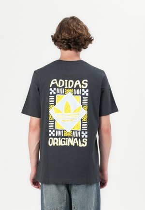 Camiseta gris oscuro de manga corta, que presenta un gran diseño gráfico en amarillo y blanco con el logo de Adidas y patrones geométricos en la parte posterior.