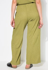 Wijdere broek in een gemêleerd olijfgroene stof met subtiele metallic draden, voorzien van een elastische tailleband en een minimalistisch design.