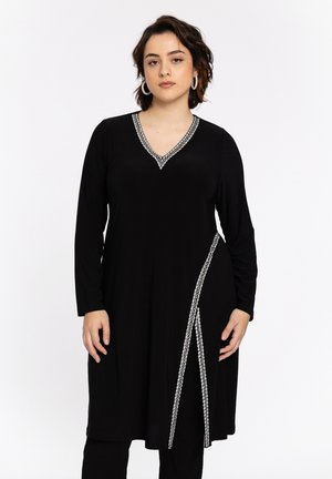 Zwarte jurk met lange mouwen en een V-hals, met zilveren kettingachtige afwerking langs de halslijn en een diagonale accent aan de ene kant.