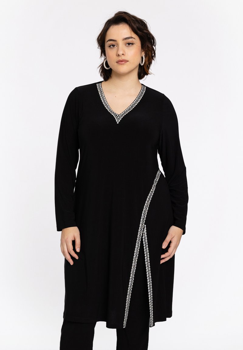 Zwarte jurk met lange mouwen en een V-hals, met zilveren kettingachtige afwerking langs de halslijn en een diagonale accent aan de ene kant.