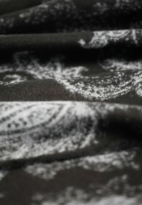Schwarzer Stoff mit weißen Blumenmustern, der eine weiche Textur und sanfte Falten zeigt, wobei das filigrane Design und die Tiefe des Materials betont werden.