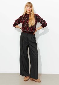 Pull en tricot avec motif losanges bordeaux et rose ; associé à un pantalon gris taille haute à jambes larges et des chaussures marron clair à lacets.