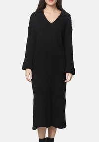 Vestito nero a maglia a coste con scollo a V e colletto. Maniche lunghe con polsini. Lunghezza a metà polpaccio e tessuto strutturato.