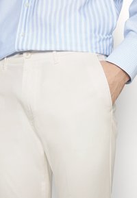 Jasne, teksturowane spodnie o prostym kroju, z przednimi kieszeniami i zapinane na guzik, zestawione z niebiesko-białą koszulą w paski.