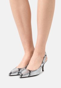 Zapatos de tacón alto con punta afilada y un patrón de serpiente en plata y negro. Cuentan con un diseño tipo slingback y una superficie texturizada.
