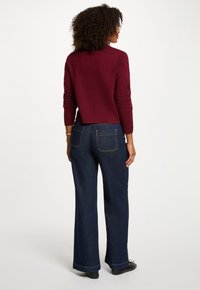 Burgundy kortärmad tröja med långa ärmar, tillsammans med vida mörk denimjeans som har bakfickor och synliga söm detaljer.