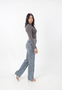 Długi rękaw, szary dopasowany top w połączeniu z jasnoniebieskimi, wysokimi, prostymi dżinsami. Modelka nosi przezroczyste sandały na obcasie.